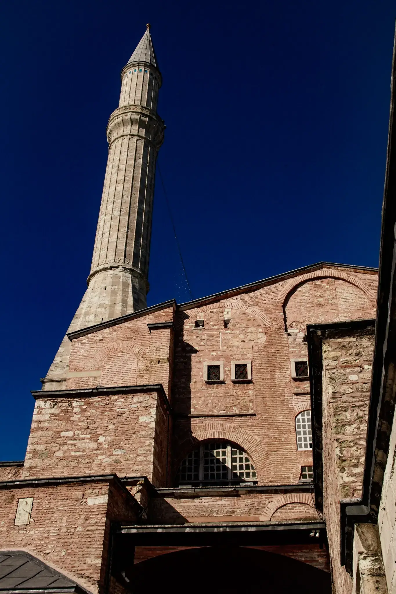 Un minarete contra un cielo azul despejado, con su balcón y su remate bajo una luz nítida.